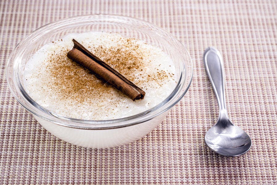Arroz doce cremoso em tigela de vidro com canela em pau e pó