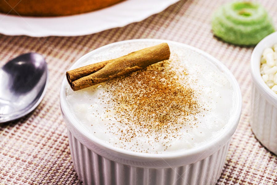 Arroz doce em tigela branca com canela em pau e pó sobre mesa rústica