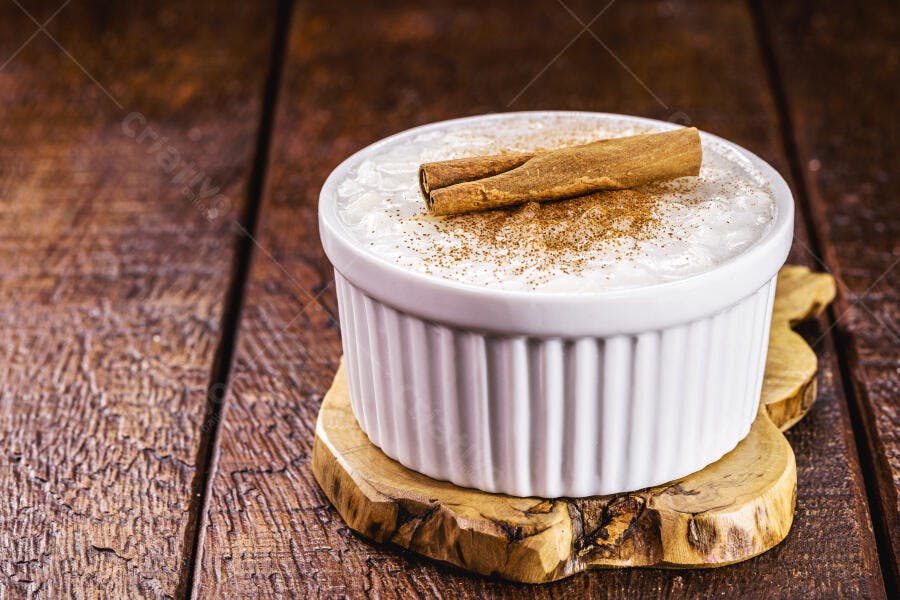 Arroz doce em ramekin branco com canela em pau sobre mesa de madeira rústica