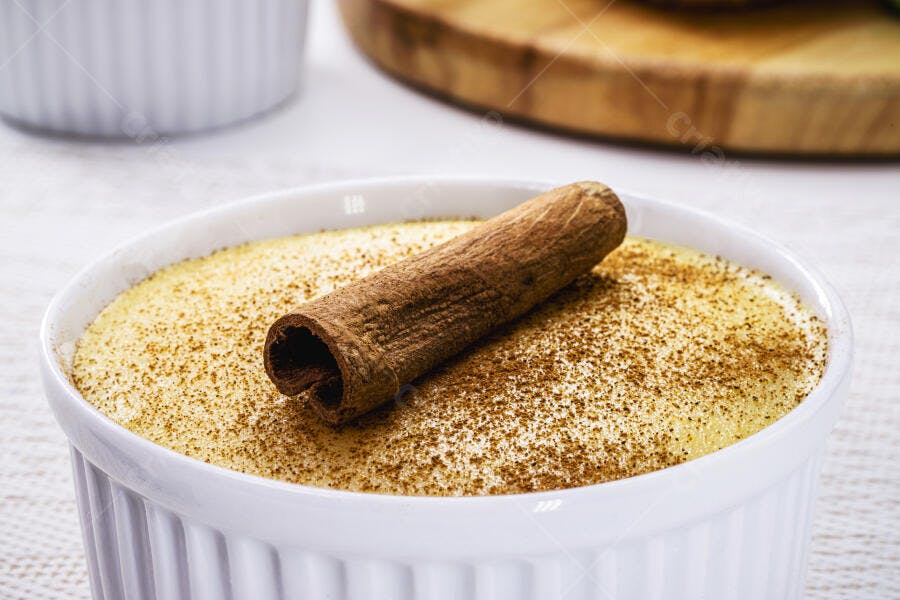 Pudim cremoso com canela em tigela branca sobre mesa clara