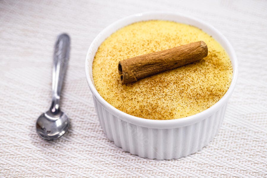 Pudim de milho amarelo com canela em rama e pó em tigela branca