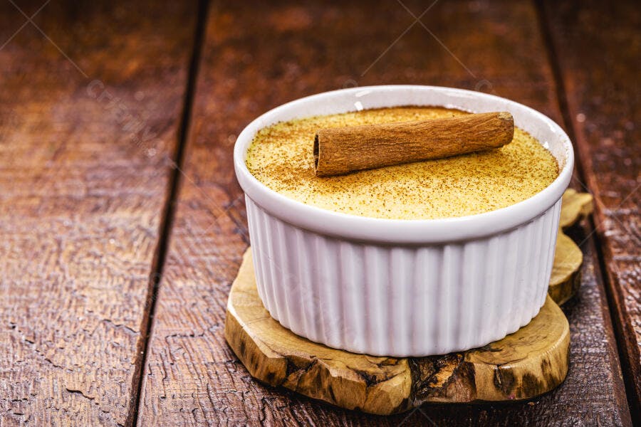 Doce cremoso de baunilha com canela em pau e pó em ramequim branco sobre madeira rústica
