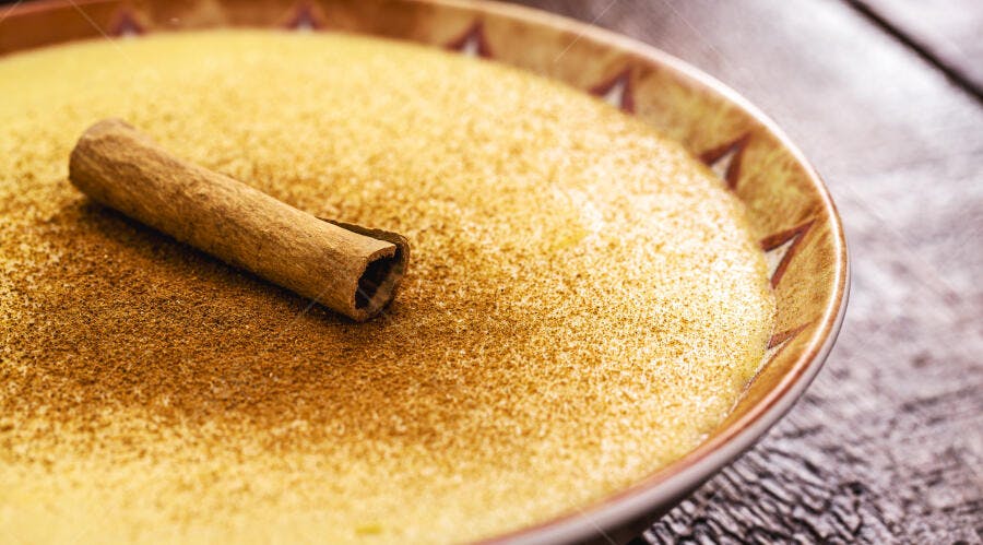 Curau de milho cremoso com canela em pau e pó em tigela rústica