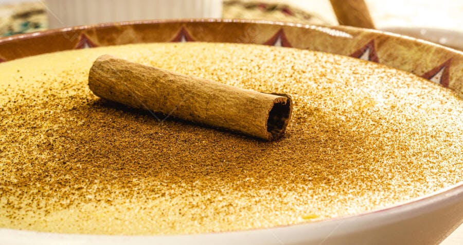 Curau de milho cremoso com canela em pó e pau em tigela decorada