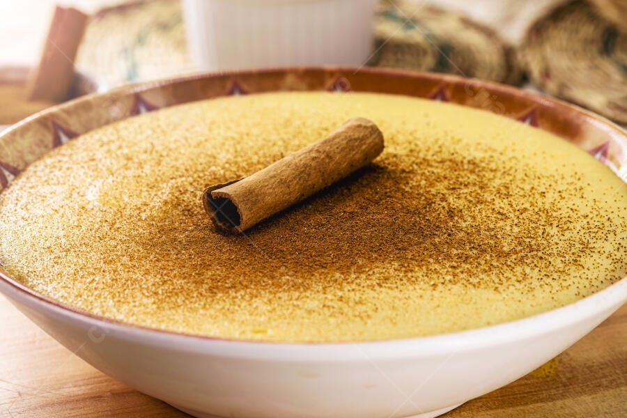 Curau de milho cremoso em tigela branca com canela em pó e pau