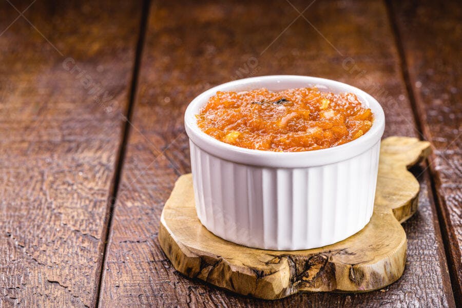 Doce de abóbora laranja em tigela branca sobre mesa de madeira rústica