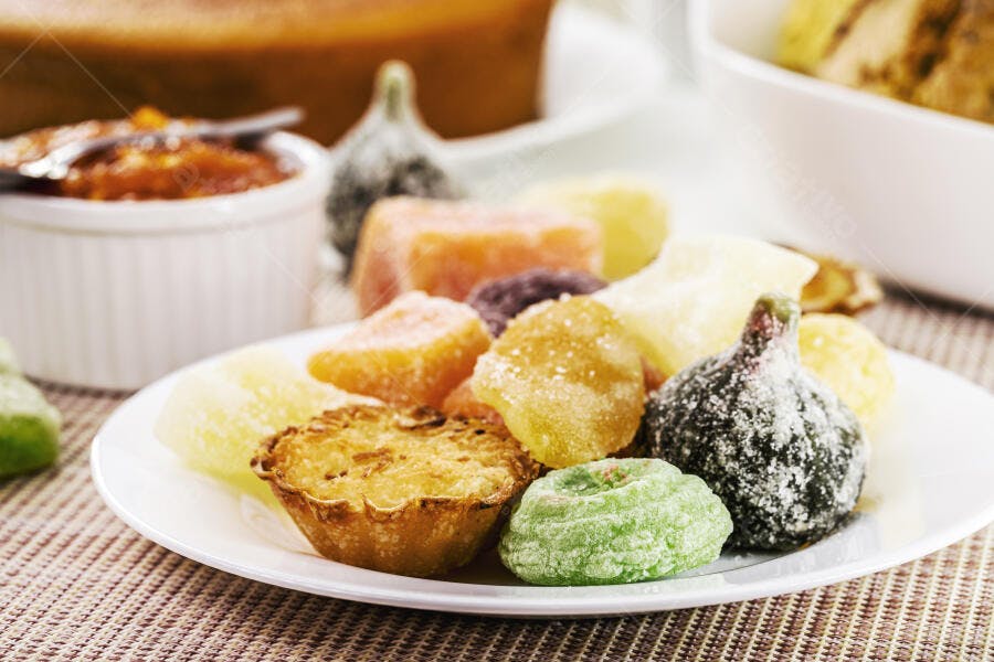 Doces cristalizados e quindim em prato branco sobre mesa coloridos