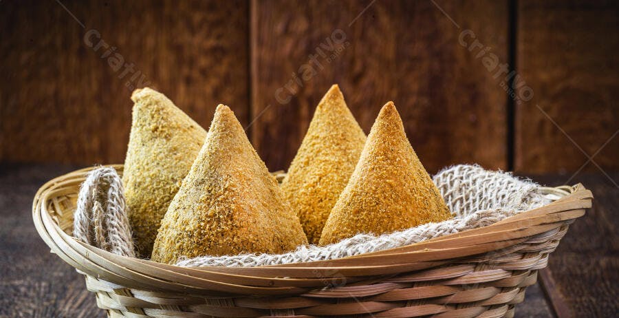 Coxinhas douradas em cesta de vime sobre mesa de madeira rústica