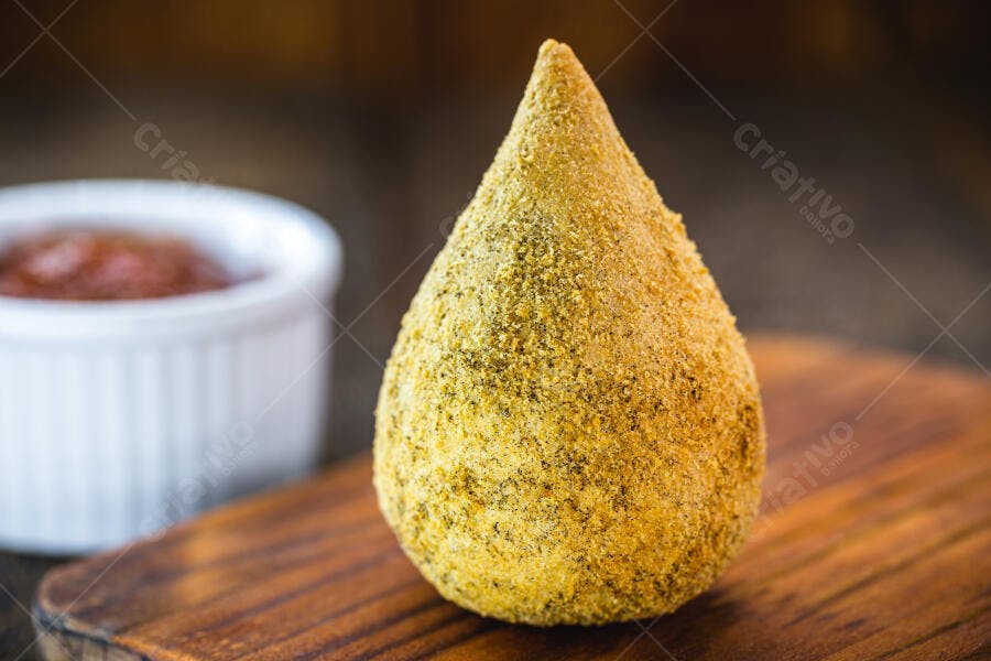 Coxinha dourada crocante em tábua de madeira com molho de pimenta