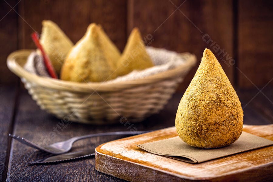 Coxinha dourada crocante em tábua de madeira rústica com talheres