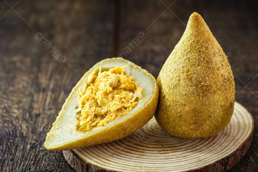 Coxinha de frango frita e cortada recheada em tábua de madeira rústica