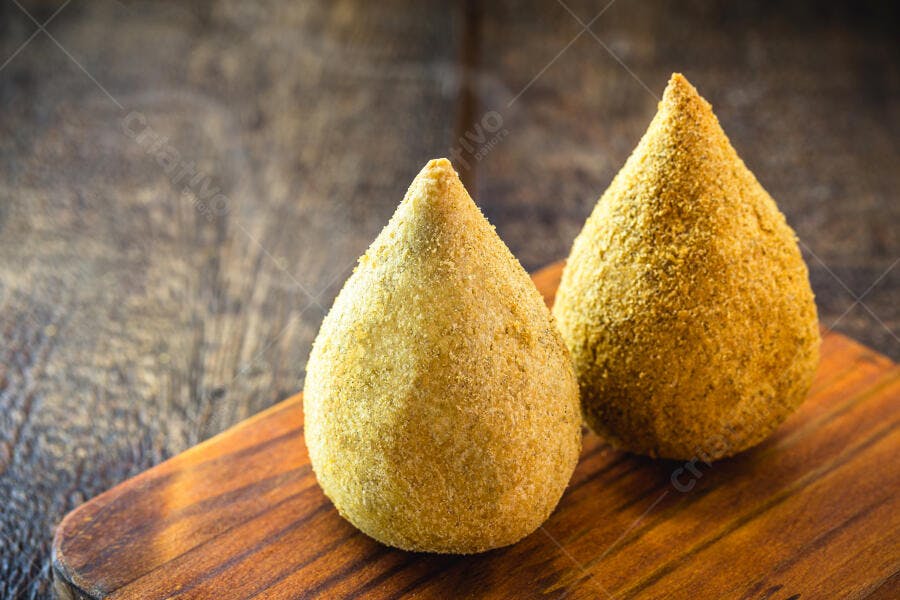 Duas coxinhas de frango empanadas crocantes sobre tábua de madeira