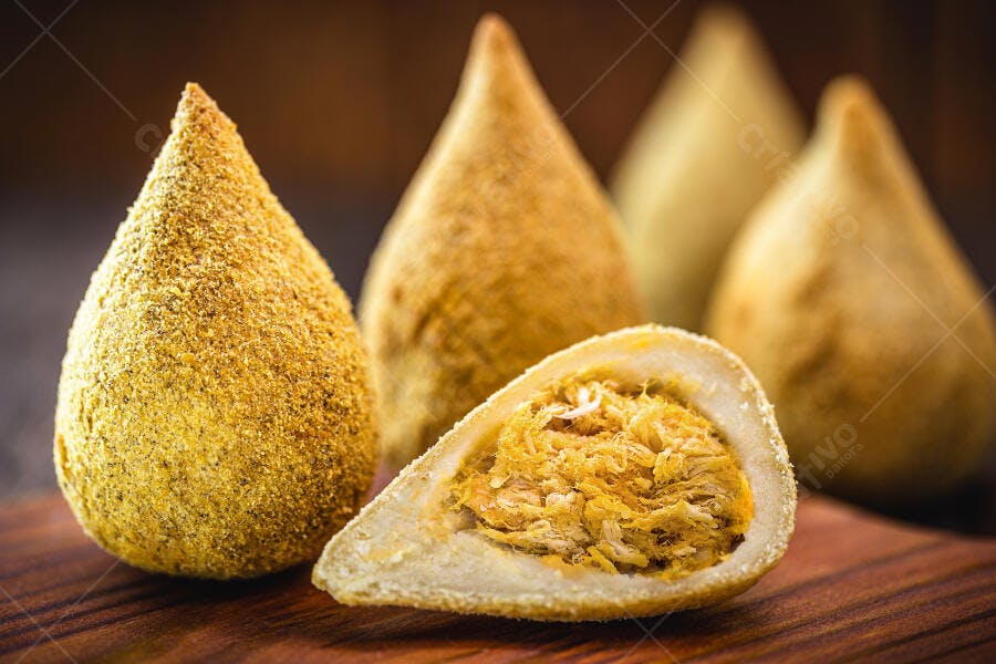 Coxinhas brasileiras douradas com recheio de frango desfiado em mesa de madeira rústica