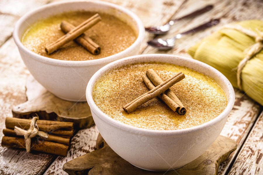 Curau de milho amarelo em tigelas brancas com canela em madeira rústica