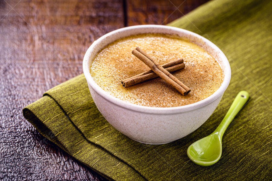 Doce de milho cremoso com canela e colher verde em mesa de madeira rústica