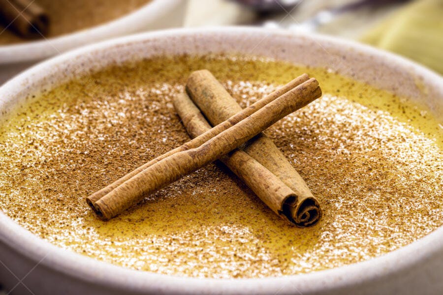 Doce cremoso amarelo com canela em pau e em pó servido em tigela clara