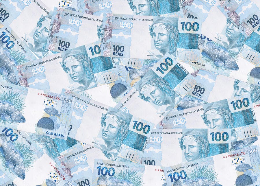 Cédulas de cem reais brasileiras espalhadas em fundo de dinheiro azul