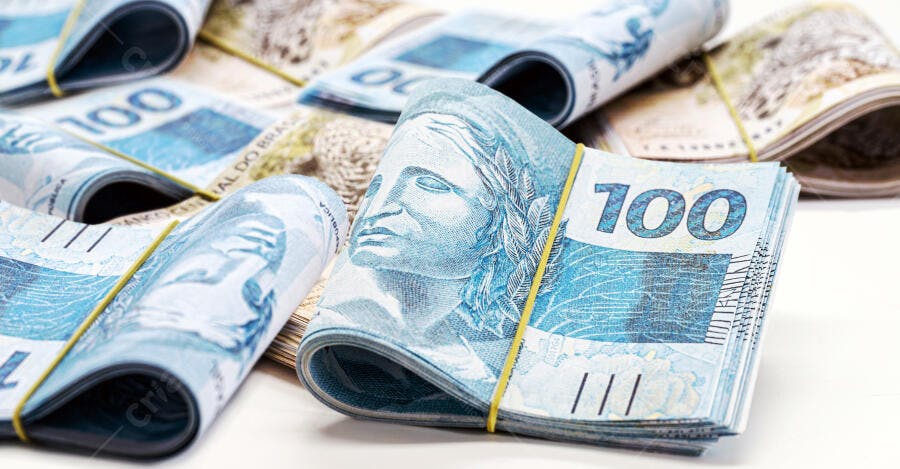 Cédulas de cem reais azuis empilhadas e enroladas com elásticos amarelos