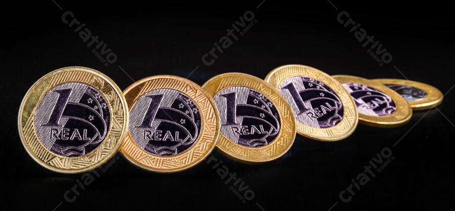 Moedas de 1 Real brasileiro douradas e prateadas em fundo escuro