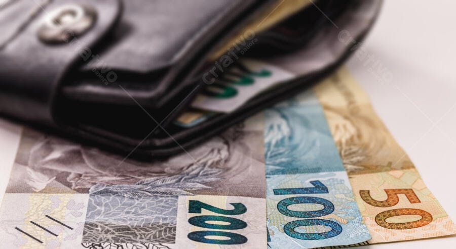 Carteira preta com notas de Real 200, 100 e 50 em fundo branco