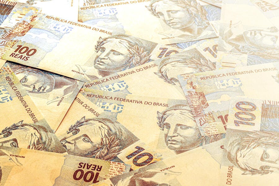 Cédulas de Reais brasileiras espalhadas fundo claro com notas de 100 e 10