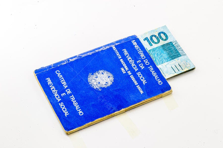 Carteira de Trabalho azul com nota de cem reais simbolizando emprego e salário