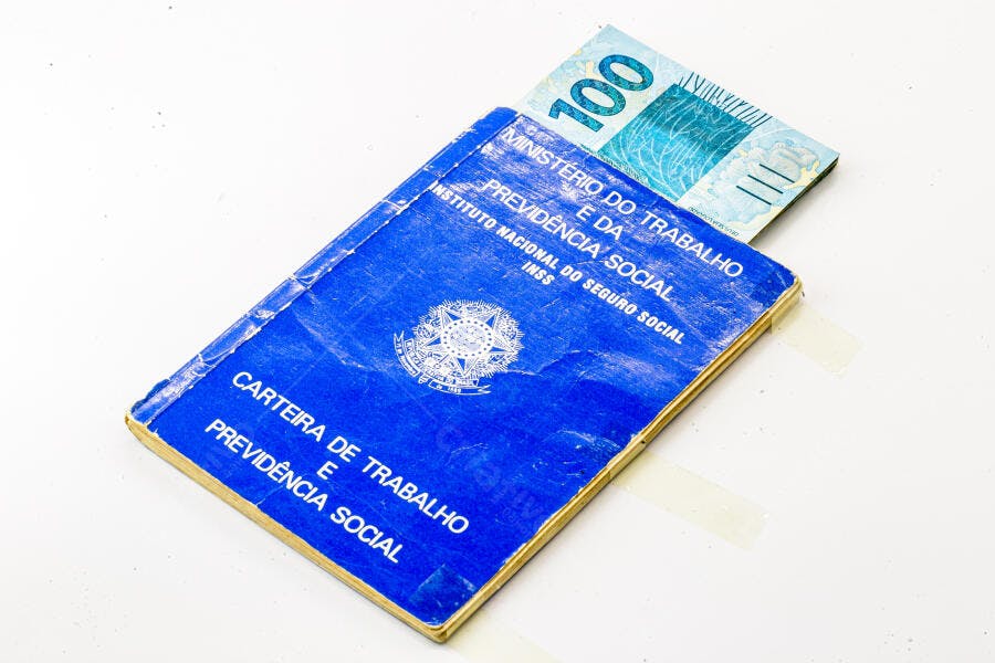 Carteira de Trabalho azul com nota de cem reais representando economia brasileira