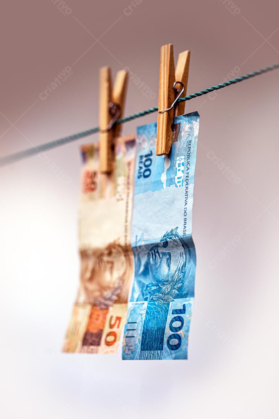 Cédulas de dinheiro brasileiro de 50 e 100 reais penduradas no varal com prendedores