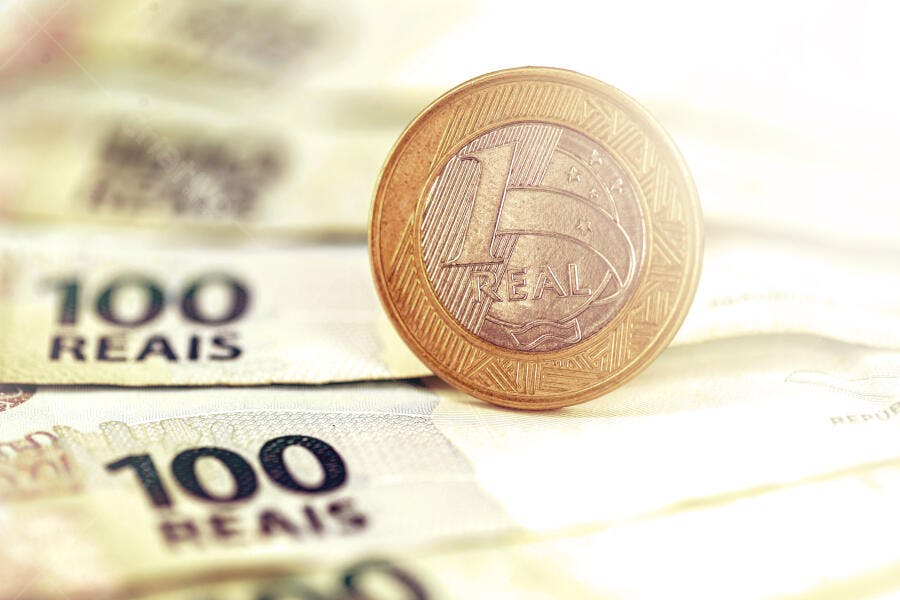 Moeda brasileira de 1 Real sobre notas de 100 Reais em luz dourada