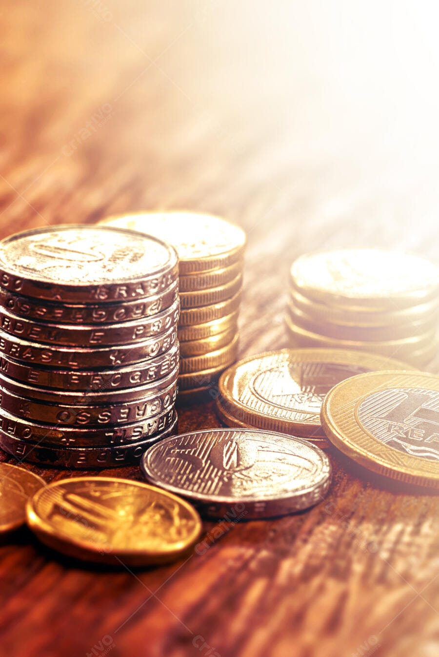 Moedas de Real brasileiras empilhadas e espalhadas sobre madeira com reflexo dourado