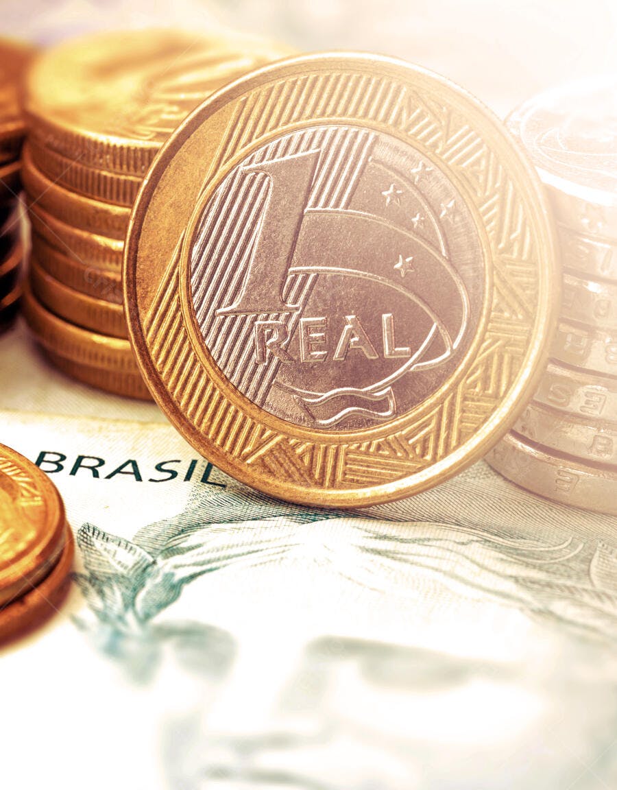 Moeda de 1 Real brasileira dourada e prateada com outras moedas e cédula