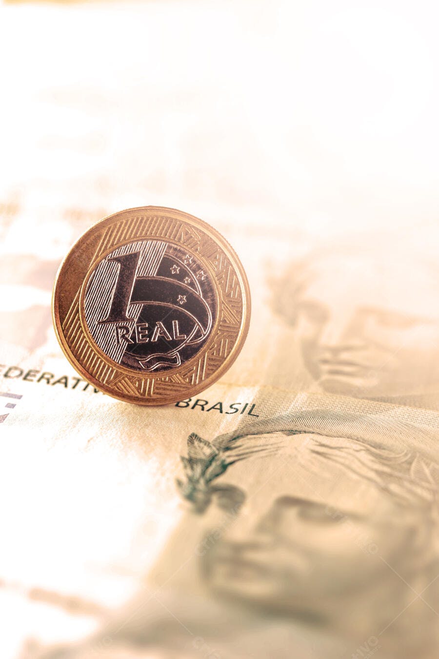 Moeda de 1 Real dourada em close-up sobre nota brasileira de dinheiro economia