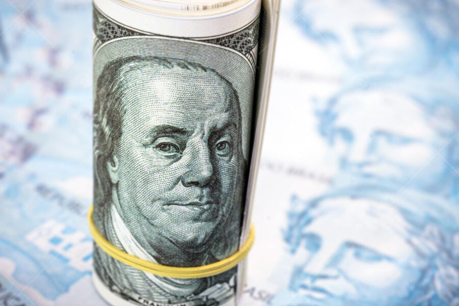 Dólares americanos enrolados com borracha em fundo de reais brasileiros