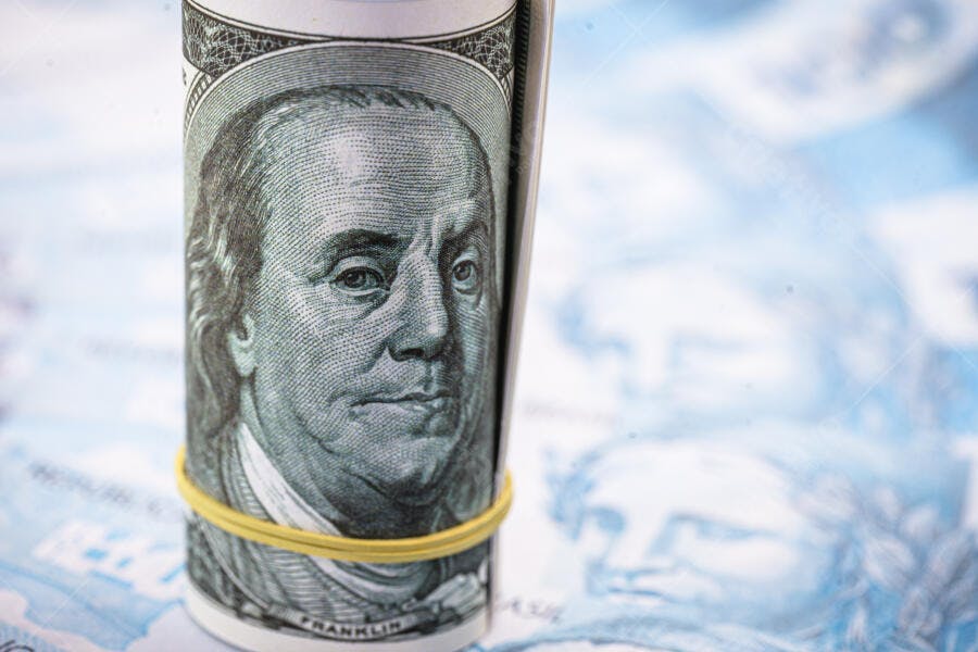 Dólar americano enrolado com Ben Franklin em foco sobre notas de Real azuis