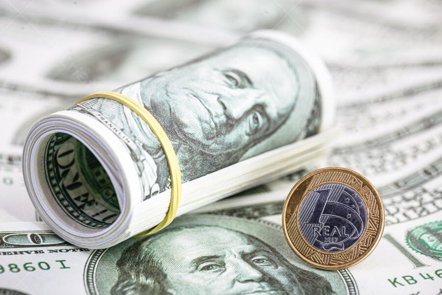 Dólar americano enrolado com moeda de Real brasileiro e notas no fundo