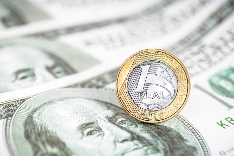 Moeda de 1 Real brasileira sobre notas de dólar americano