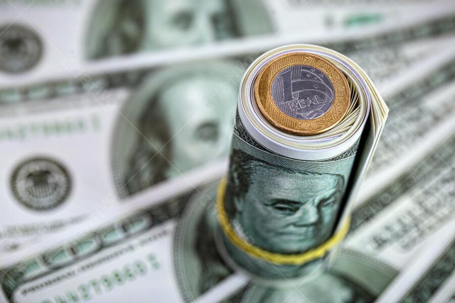 Dinheiro dólar enrolado com moeda real brasileira em fundo de notas verdes