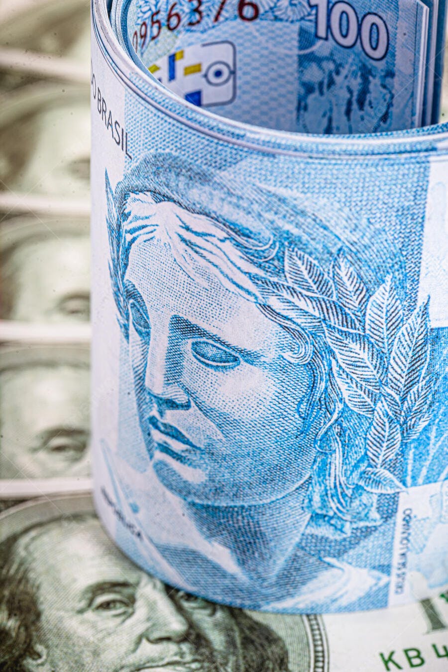 Cédula de 100 Reais azul enrolada sobre dólares americanos