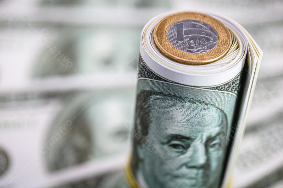 Cédulas de dólar enroladas com moeda de 1 Real no topo economia global
