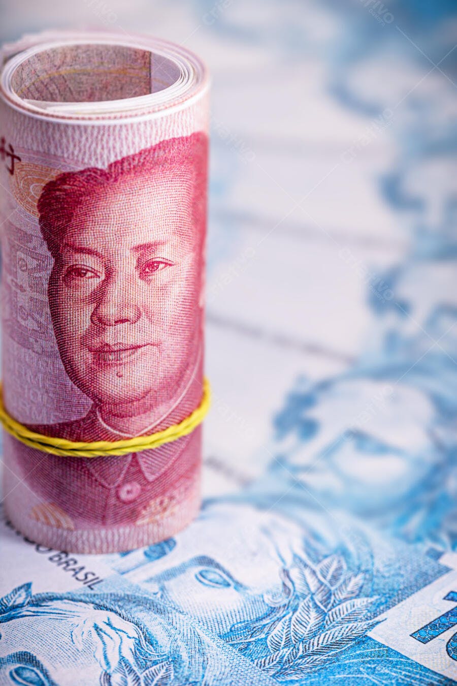 Notas de Yuan chinês enroladas com retrato de Mao Zedong sobre Reais brasileiros azulados