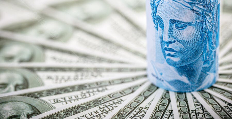 Cédula de real brasileira enrolada sobre notas de dólar americano espalhadas