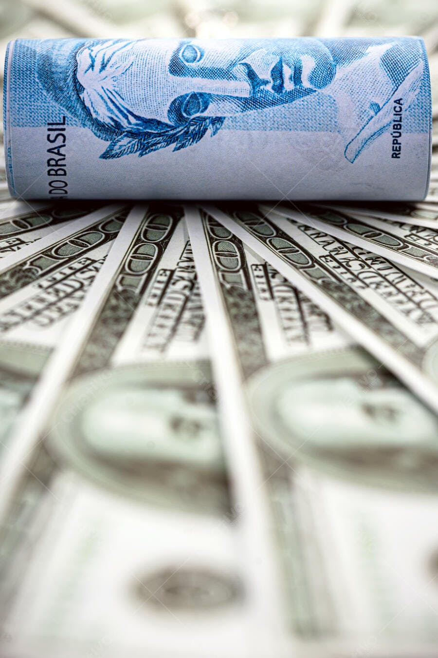 Cédula de Real azul enrolada sobre dólares americanos comparando moedas