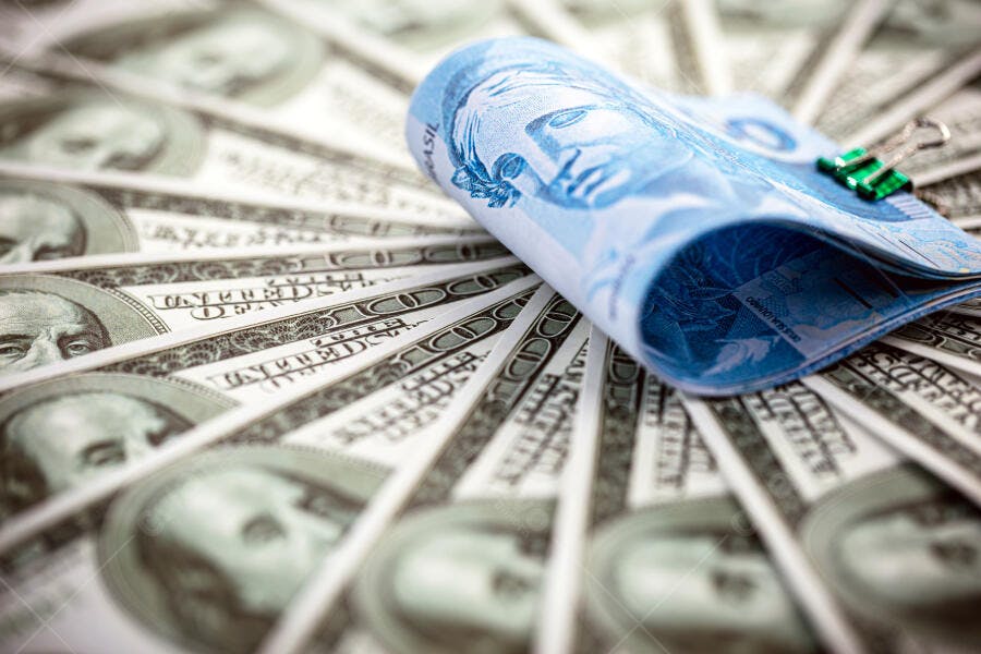 Cédulas de dólar e real com clipe verde representando finanças globais
