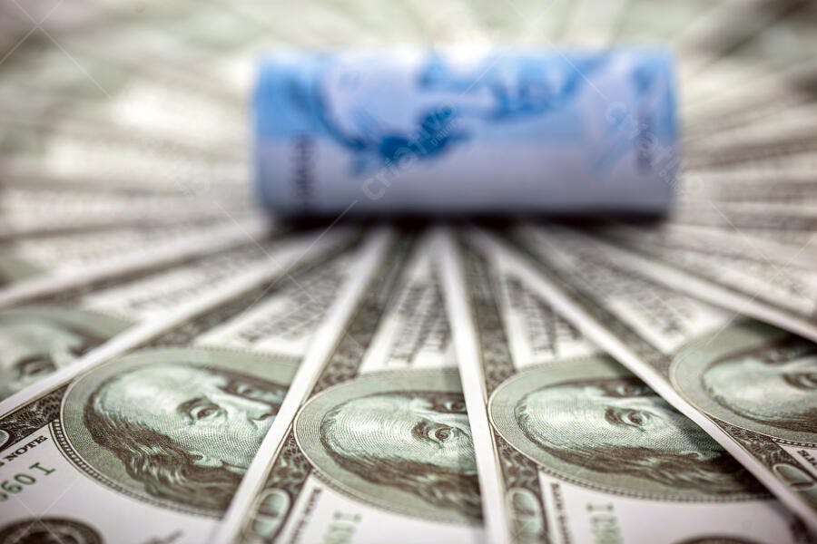 Notas de dólar americano em leque com nota de real brasileira desfocada azul e verde
