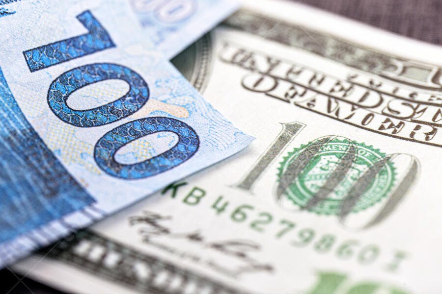 Cédulas de 100 reais e 100 dólares americanos sobrepostas em close-up