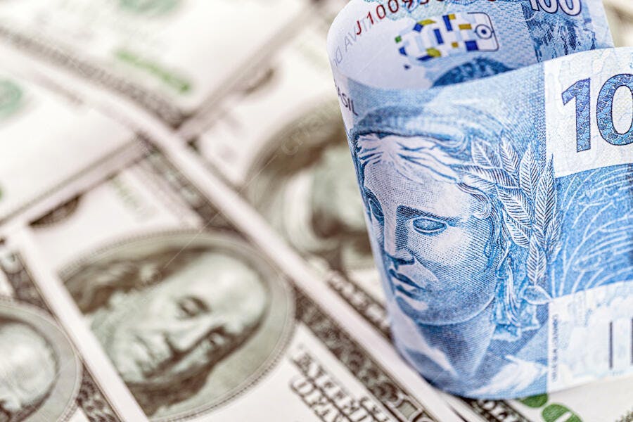 Notas de cem reais enroladas sobre cédulas de cem dólares americanos
