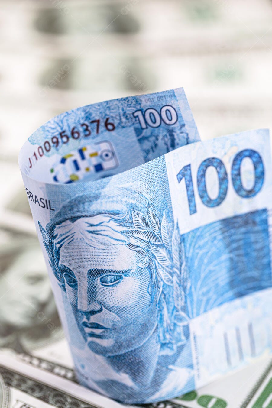Nota de 100 Reais azul dobrada com Efígie da República sobre dólares americanos