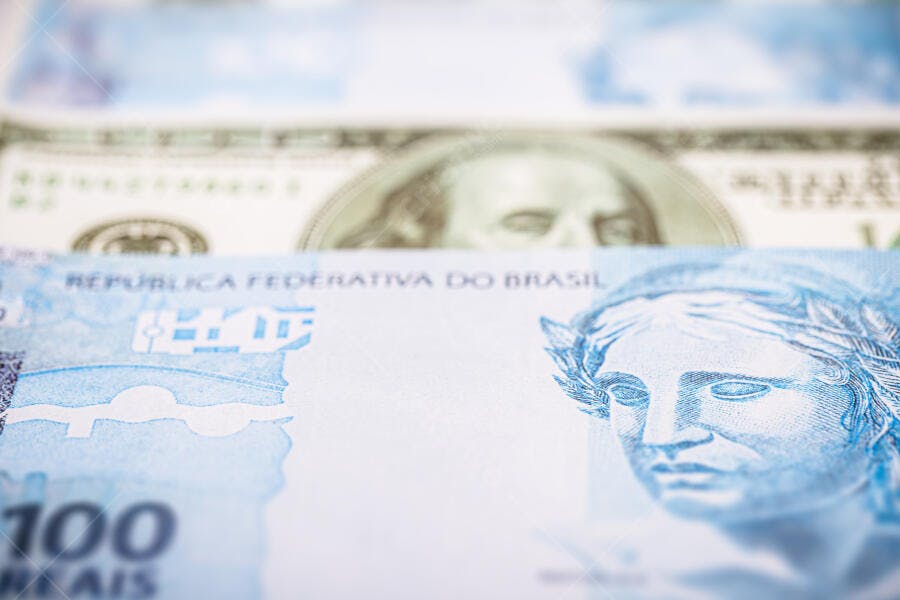 Cédula de cem reais azul com dólar americano em segundo plano foco financeiro