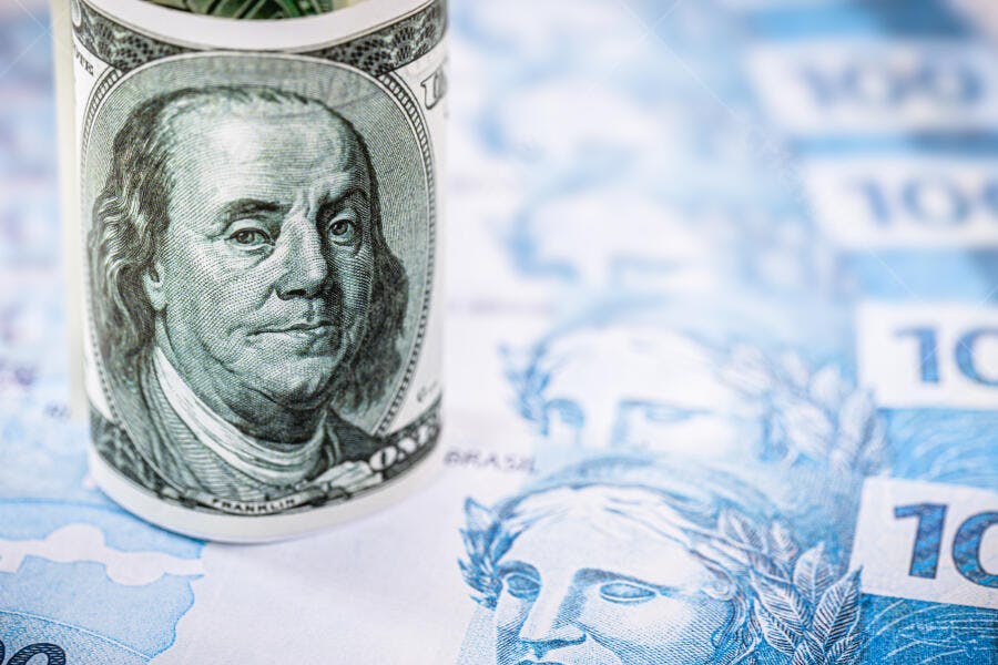 Dólar americano enrolado sobre notas de cem reais brasileiras