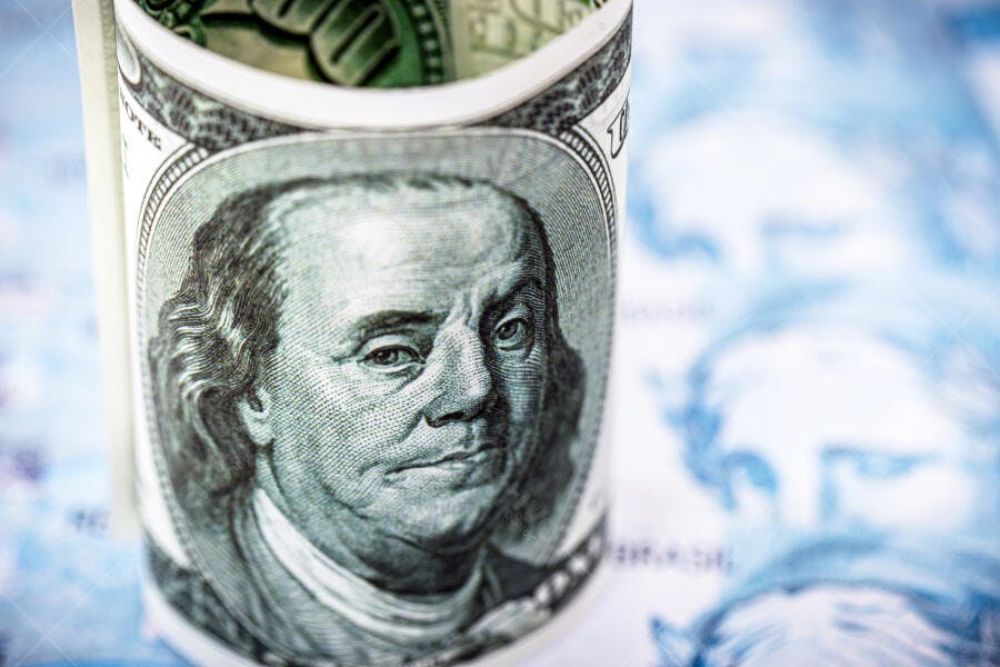 Cédula de cem dólares enrolada com Benjamin Franklin em fundo azul